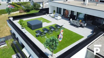 Große Dachterrasse mit Kunstrasen, Whirlpool und Essbereich, umgeben von grüner Landschaft.