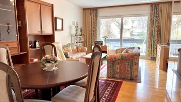 Geräumiger Wohn- und Essbereich mit Holzmöbeln, Parkettboden und Zugang zum Balkon.