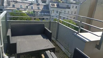 Möblierter Balkon mit Rattanmöbeln und Blick über die Dächer der Stadt.
