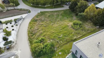 Luftaufnahme eines unbebauten Grundstücks mit Zufahrtsstraße und angrenzendem modernen Gebäude.