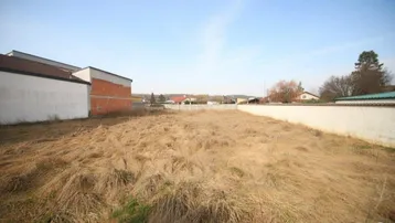 Leeres Grundstück mit trockenem Gras und angrenzenden Gebäuden unter klarem blauem Himmel.