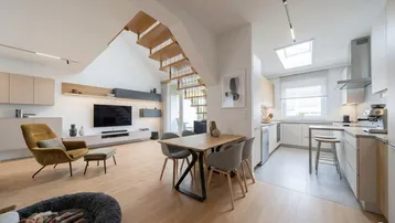 Heller, offener Wohn- und Essbereich mit moderner Küche, Holztreppe und Dachfenster.