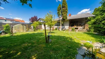 Großer, gepflegter Garten mit Rasenfläche, kleinem Teich und Gewächshaus hinter dem Haus.