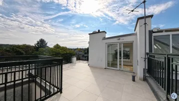 Große Dachterrasse mit Fliesenboden und Blick auf die Umgebung unter blauem Himmel.