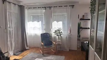 Helles Wohnzimmer mit Holzboden, einem Sessel und Fitnessgerät, durchflutet von Tageslicht.