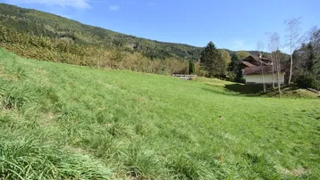 Weitläufige Grünfläche mit Blick auf die umliegende Berglandschaft und ein Wohnhaus im Hintergrund.