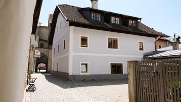 Historisches Gebäude mit heller Fassade und traditionellen Holzfenstern an einem gepflasterten Weg.