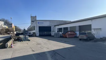 Außenansicht eines Industriegebäudes mit großem Parkplatz und Laderampen unter blauem Himmel.