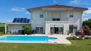 Haus mit Pool, Terrasse und Garten unter blauem Himmel und Solaranlage auf dem Dach.