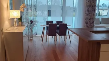 Heller offener Wohn- und Essbereich mit Holzboden, modernen Möbeln und Zugang zum Balkon.