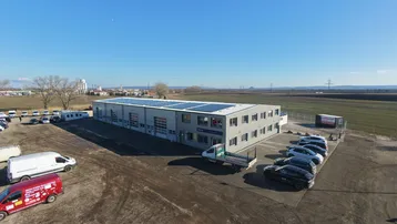 Luftaufnahme eines modernen Gewerbegebäudes mit Solarpaneelen auf dem Dach und umliegenden Parkplätzen.