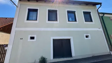 Fassade eines traditionellen Wohnhauses mit mehreren Fenstern und Rollläden unter blauem Himmel.