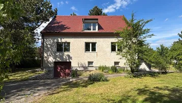 Traditionelles Einfamilienhaus mit rotem Dach, integrierter Garage und großem Gartenbereich.