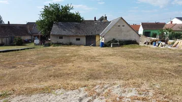 Blick auf ein trockenes Grundstück mit älteren Nebengebäuden und umliegenden Häusern in ländlicher Umgebung.