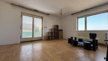 Geräumiges Wohnzimmer mit Holzparkett, großen Fenstern und Zugang zu einem Außenbereich.