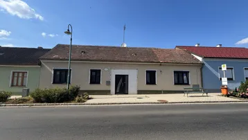 Einfaches Wohnhaus mit heller Fassade und Satteldach an einer Straße gelegen.