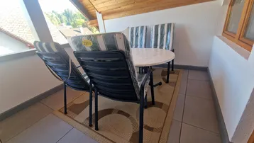 Sonniger Balkon mit Holzdach, Fliesenboden und Blick auf die umliegende Landschaft.