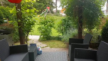 Gemütliche Terrasse mit Sitzgelegenheiten und Blick auf den Garten mit Kinderspielplatz.