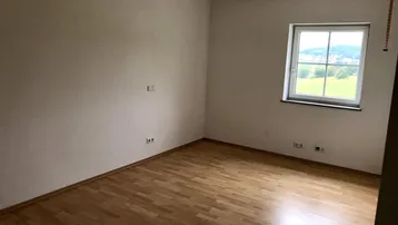 Heller Raum mit Laminatboden und einem Fenster, das einen schönen Blick ins Grüne bietet.