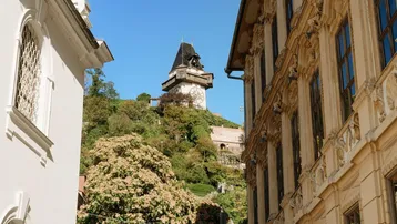 Historisches Gebäude mit Blick auf den Uhrturm am Schlossberg in Graz unter blauem Himmel.