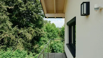 Kleiner Balkon mit Glasgeländer und weitem Blick in die umliegende Waldlandschaft.