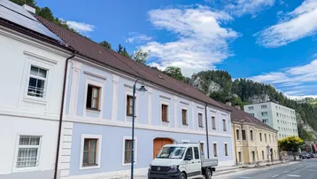 Historisches Gebäude mit hellblauer Fassade und Photovoltaikanlage auf dem Dach an einer Straße.