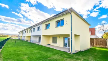 Reihenhäuser mit hellgelber Fassade und privatem Gartenbereich unter blauem Himmel.