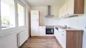 Helle Einbauküche mit Holzoptik-Arbeitsplatten, modernen Geräten und großem Fenster.