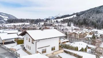 Winterliche Ansicht eines weißen Hauses in einer verschneiten Berglandschaft mit vielen weiteren Gebäuden.