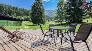 Große Holzterrasse mit Gartenmöbeln und weitem Blick auf die umliegende Natur und Berge.