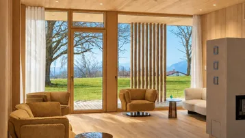Lichtdurchflutetes Wohnzimmer mit Holzboden, modernen Sesseln und Kaminofen mit Blick ins Grüne.