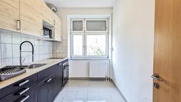 Funktionale Küche mit dunklen Unterschränken, hellen Oberschränken, Fliesenboden und Fenster.