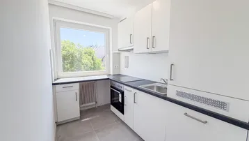 Helle Küche mit weißen Schränken, dunkler Arbeitsplatte und Fenster mit Blick ins Grüne.