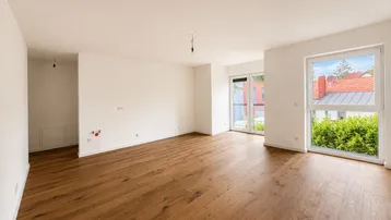 Helles, unmöbliertes Zimmer mit Holzboden und großen Fenstern, die viel Tageslicht hereinlassen.