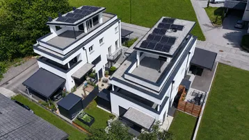 Moderne weiße Gebäude mit Flachdächern, Solaranlagen und kleinen Gärten in einer Wohnsiedlung.