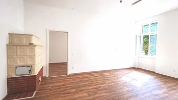 Helles Zimmer mit Holzboden und traditionellem Kachelofen, ideal als Wohn- oder Schlafbereich.