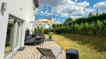 Große Holzterrasse mit modernen Gartenmöbeln und Sonnenschirm, umgeben von einem gepflegten Rasen und Hecken.