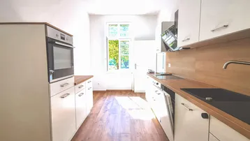 Moderne Einbauküche mit weißen Schränken, Holzarbeitsplatten und integrierten Geräten.