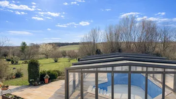 Großer Außenbereich mit überdachtem Pool und weitem Blick in die grüne Landschaft unter blauem Himmel.