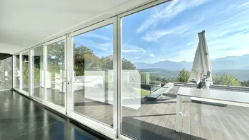 Innenraum mit raumhohen Fenstern, die einen Panoramablick auf die Terrasse und die Berge ermöglichen.