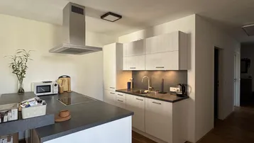 Moderne Küche mit Kochinsel, Dunstabzugshaube und Holzboden, ideal für offenes Wohnen.