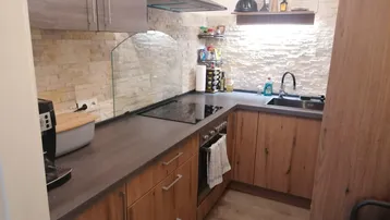 Moderne Küche mit Holzfronten, dunkler Arbeitsplatte und Steinoptik-Fliesen an der Wand.