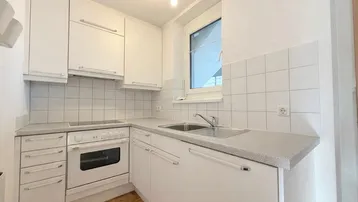 Kompakte weiße Einbauküche mit Elektroherd, Spüle und Fenster.