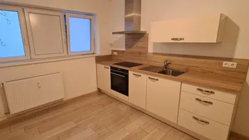 Moderne Küche mit weißen Schränken, Holzarbeitsplatte, Dunstabzugshaube und Fenster.