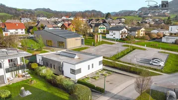 Luftaufnahme eines modernen Gebäudekomplexes in einer ländlichen Umgebung mit weiteren Häusern und viel Grün.