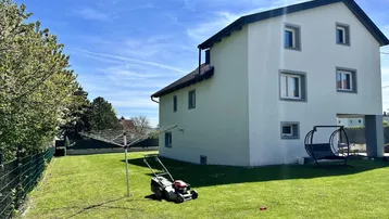Gepflegter Garten mit Rasenfläche, Wäschespinne und Rasenmäher vor dem Wohnhaus.