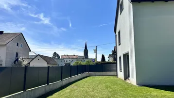 Gartenbereich mit Rasenfläche und Blick auf die Nachbarschaft mit einem Kirchturm in der Ferne.