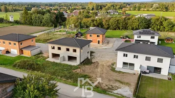 Luftaufnahme einer Neubausiedlung mit Häusern in verschiedenen Bauphasen und ländlicher Umgebung.