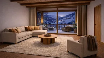 Gemütliches Wohnzimmer mit Holzbalkendecke, großem Sofa und Panoramablick auf die verschneiten Berge.
