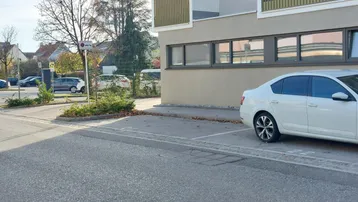 Moderne Gebäudefassade mit Balkonen und Außenparkplätzen, umgeben von Bäumen und Grünflächen.